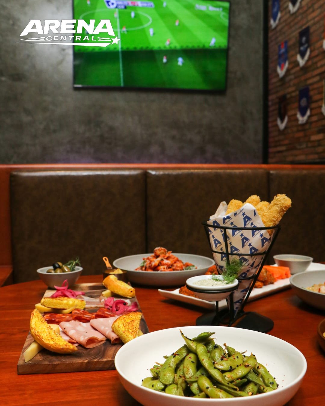 Sharing platters, edamame and fried bites on a table at Arena Central, with live football on the screen behind
